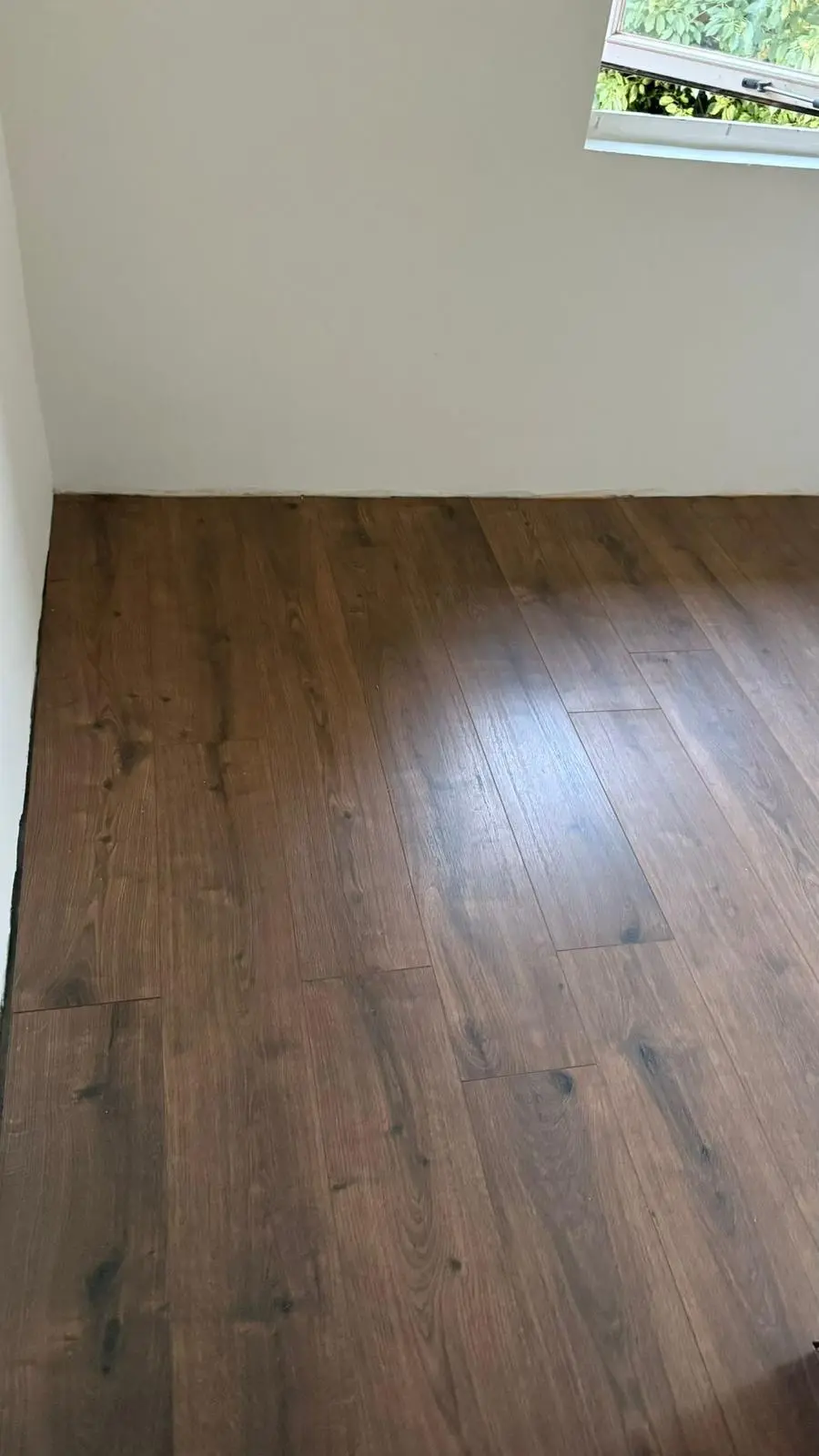 Strak gelegde donkerbruine laminaatvloer in een slaapkamer met een schuine wand